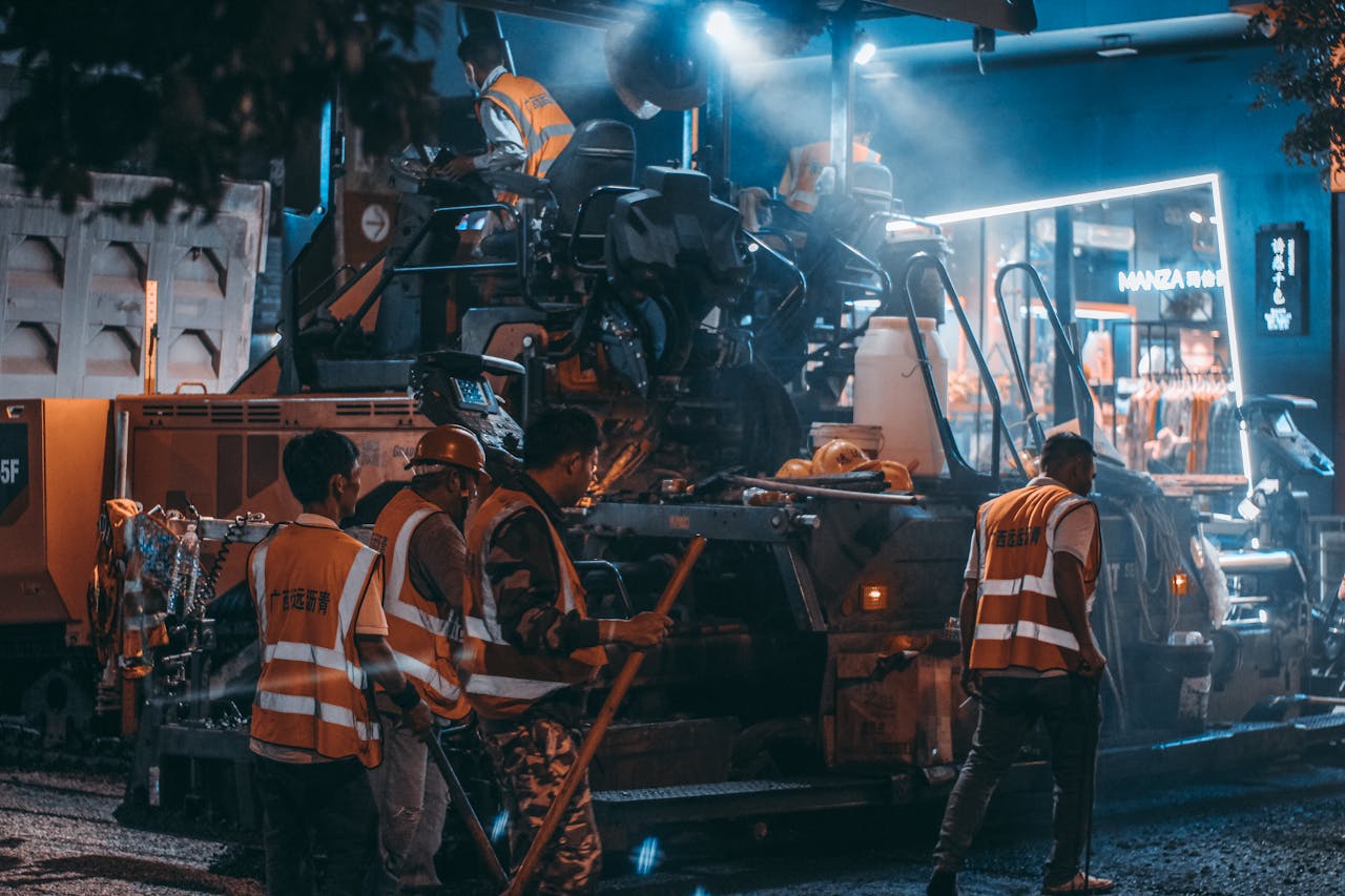why-choose-us Road construction crew at work with machinery and lights during the night.