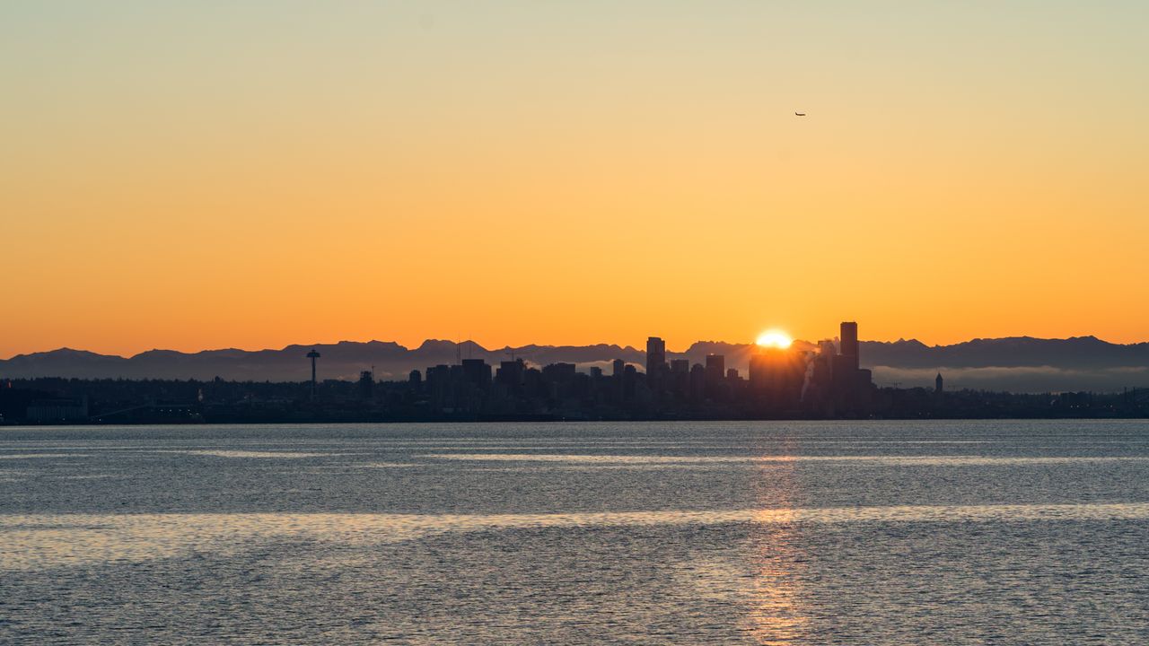 our-story Breathtaking view of Seattle skyline at sunset with vibrant orange hues over calm waters.
